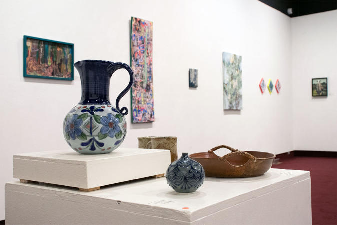 Sculpted Art Pieces on a Display Table with Paintings Hanging in Background