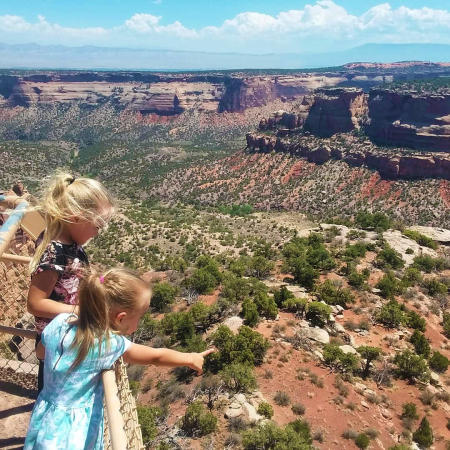 Two girls standing and pointing out across the Colorado National Monument